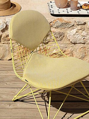 Yellow woven patio chair on wooden deck with stone wall background
