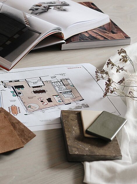 Interior design planning with material samples, floor plan, and open magazines on a desk