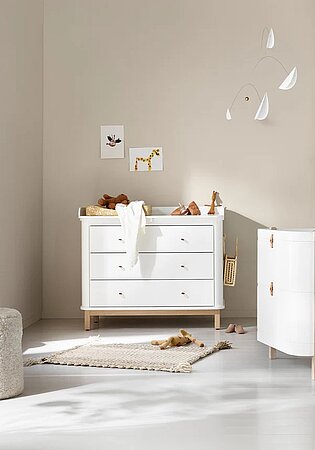 Modernes Babyzimmer mit weißer Wickelkommode, Teppich und Holzspielzeug in natürlichem Licht