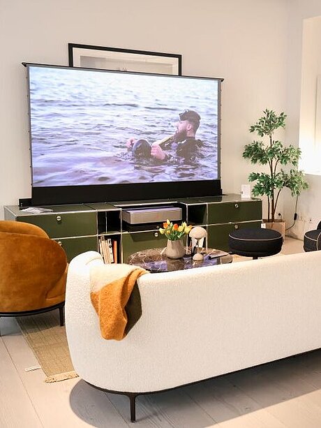 Modern living room with white couch, projector screen, and potted plant