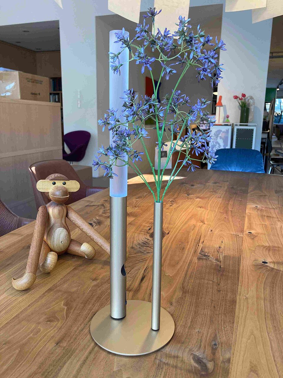 Moderne Metallvase mit lila Kunstblumen auf Holztisch neben Holzfigur in Wohnzimmer