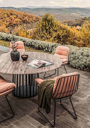Runder Terrassentisch mit rosa Stühlen und Aussicht auf herbstliche Hügellandschaft