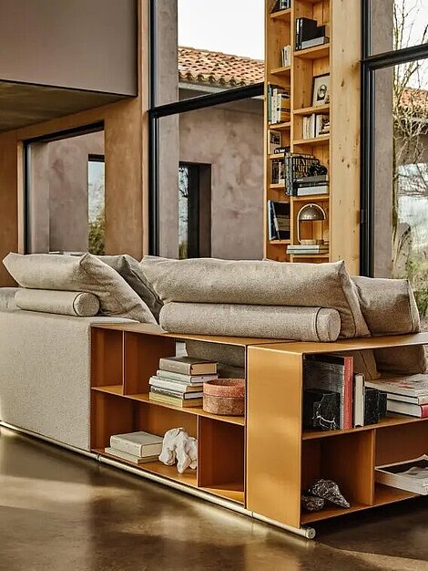 Modernes Wohnzimmer mit beiger Couch, Holzregal und großen Fenstern mit Gartenblick