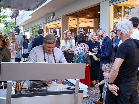 Chef preparing dough outdoors while a crowd mingles around