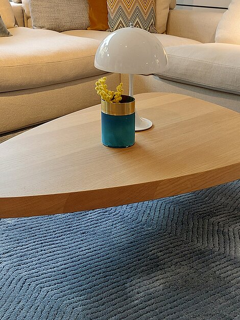 Modernes Wohnzimmer mit hellen Sofas, einem Holz-Couchtisch und Designerlampe auf blauem Teppich