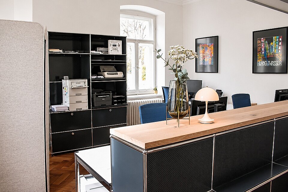 Modern office with black shelves, printer, vase, and lamp on wooden counter