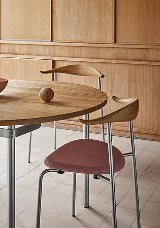 Moderner Esszimmerstuhl mit gepolsterter rosa Sitzfläche und Holzlehne an rundem Holztisch