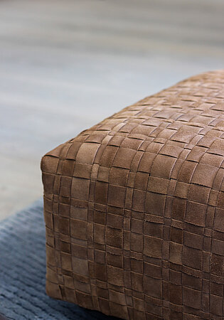 Brauner gepolsterter Hocker mit gewebtem Wildlederbezug auf blauem Teppichboden