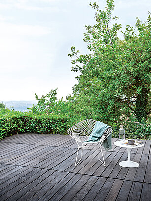Moderne Terrasse mit weißem Stuhl, Beistelltisch und Blick auf grüne Bäume und Landschaft