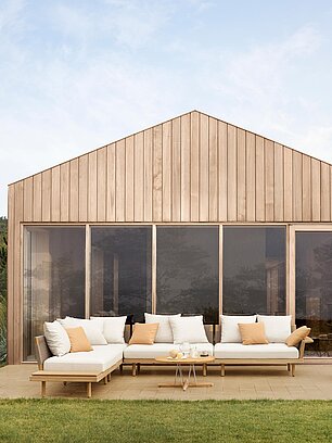 Moderne Terrasse mit weißen Gartenmöbeln vor einem Holzhaus im minimalistischen Design