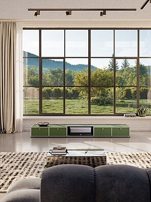 Wohnzimmer mit großen Fenstern, grauen Sofas und Blick auf grüne Landschaft