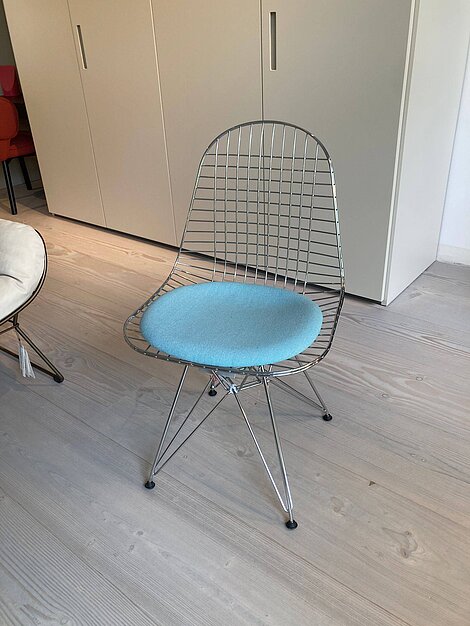 Moderner Stuhl mit Metallgitterrahmen und hellblauem Sitzkissen auf Holzfußboden