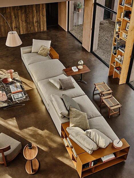 Modernes Wohnzimmer mit modularem Sofa, Bücherregal aus Holz und Designer-Beistelltischen auf Betonboden