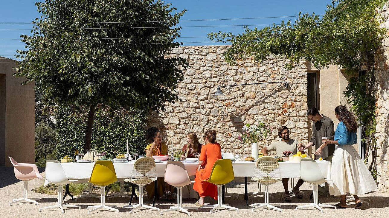 Outdoor gathering with people sitting at a white table against a stone wall backdrop